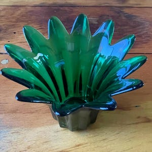 May include: A green glass vase with a starburst design. The vase is made of thick glass and has a deep green color.