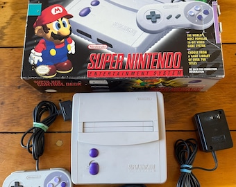 May include: A Super Nintendo Entertainment System, including the console, controller, and power adapter, is displayed. The box features Mario and Yoshi graphics. The console is gray with purple buttons. The controller is gray with purple buttons.