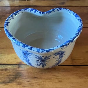 May include: A white ceramic heart-shaped bowl with a blue and white floral pattern. The bowl has a scalloped edge and is perfect for serving snacks or holding small items.