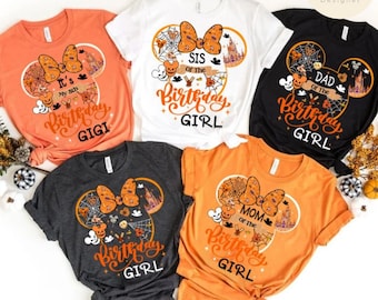 May include: Five short-sleeved t-shirts in orange, white, black, and gray, featuring a Halloween-themed design. Each shirt has a Mickey Mouse-shaped design with text that says "Birthday Girl" and other text such as "Gigi", "Sis", "Dad", and "Mom".