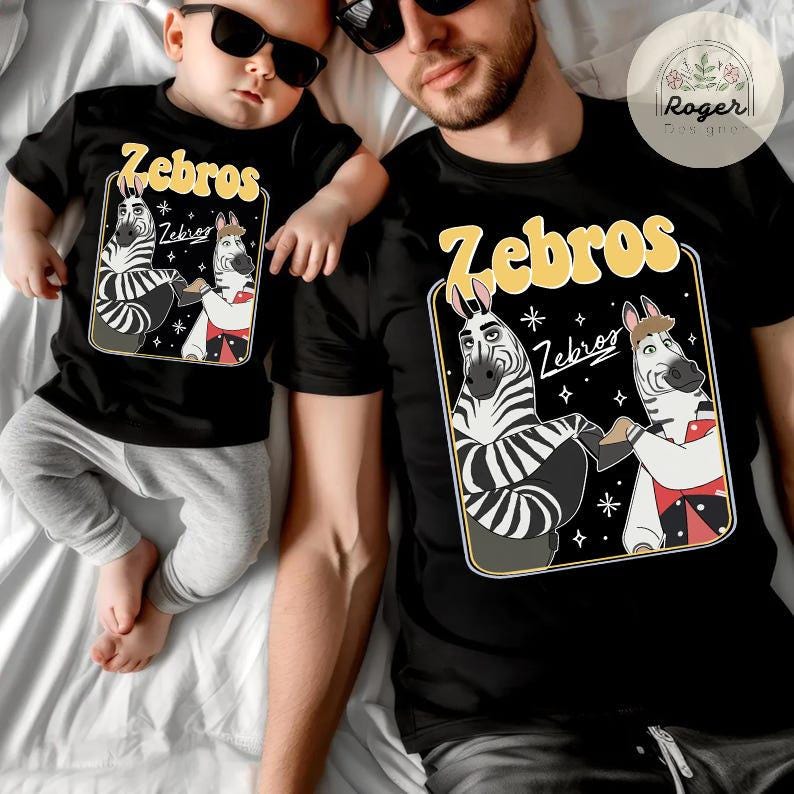 Pu&ograve; includere: T-shirt nere con la scritta "Zebros" in giallo, con un disegno di zebra dei cartoni animati. Una maglietta &egrave; indossata da un bambino, l'altra da un adulto. Entrambe le magliette hanno lo stesso disegno.