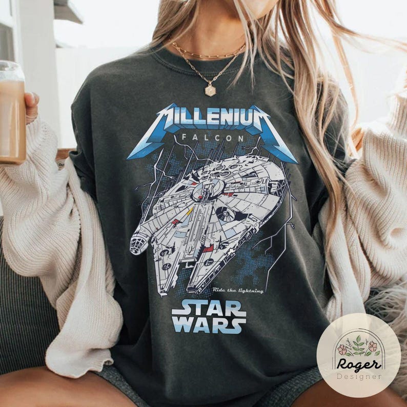 May include: A dark gray t-shirt with a graphic print of the Millennium Falcon spaceship from Star Wars. The text "Millenium Falcon" and "Star Wars" are printed on the shirt. The text "Ride the lightning" is also printed on the shirt.