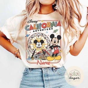 May include: Cream-colored t-shirt featuring a graphic of Mickey Mouse and a Ferris wheel, with the text "Disney California Adventure." Mickey Mouse is depicted in his classic outfit. The shirt has short sleeves and a crew neck.