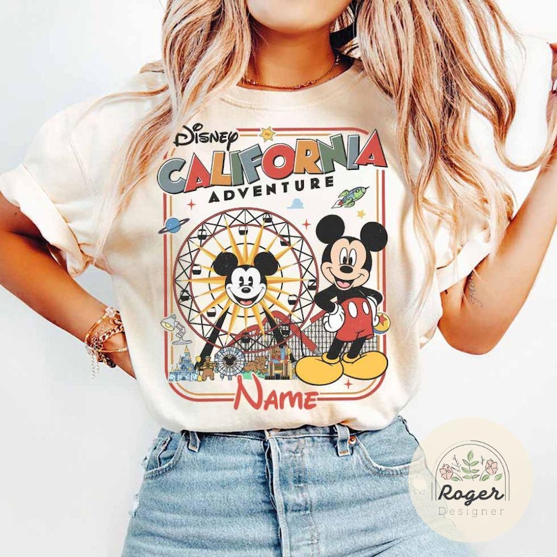 May include: Cream-colored t-shirt featuring a graphic of Mickey Mouse and a Ferris wheel, with the text "Disney California Adventure." Mickey Mouse is depicted in his classic outfit. The shirt has short sleeves and a crew neck.