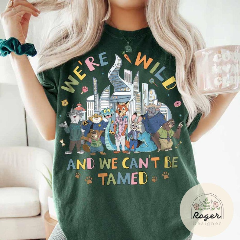 May include: Dark green t-shirt with the text "WE'RE WILD AND WE CAN'T BE TAMED" and a colorful graphic of cartoon animals and city buildings. The shirt has a crew neck and short sleeves.