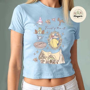 Może przedstawiać: Jasnoniebieska koszulka z fantazyjną ilustracją. Projekt zawiera dom, lustro i r&oacute;żne postacie z kresk&oacute;wek z napisem "Forest of them all". Po prawej stronie widoczne jest okrągłe logo z tekstem.