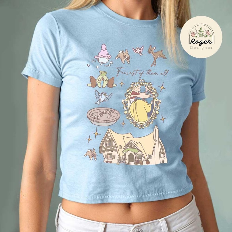 Może przedstawiać: Jasnoniebieska koszulka z fantazyjną ilustracją. Projekt zawiera dom, lustro i r&oacute;żne postacie z kresk&oacute;wek z napisem "Forest of them all". Po prawej stronie widoczne jest okrągłe logo z tekstem.