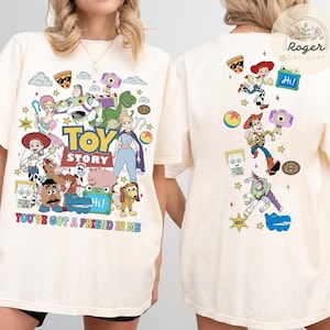 May include: An off-white t-shirt featuring a large graphic print of Toy Story characters on the front and a vertical arrangement of the same characters on the back. The front includes the text TOY STORY and YOU'VE GOT A FRIEND IN ME.