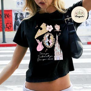 Może przedstawiać: Czarny t-shirt z kolorową grafiką przedstawiającą zamek, księżniczkę i sowę. Tekst "I know you... I walked with you... Once upon a dream" jest wydrukowany poniżej. Logo Roger Designer w prawym g&oacute;rnym rogu.