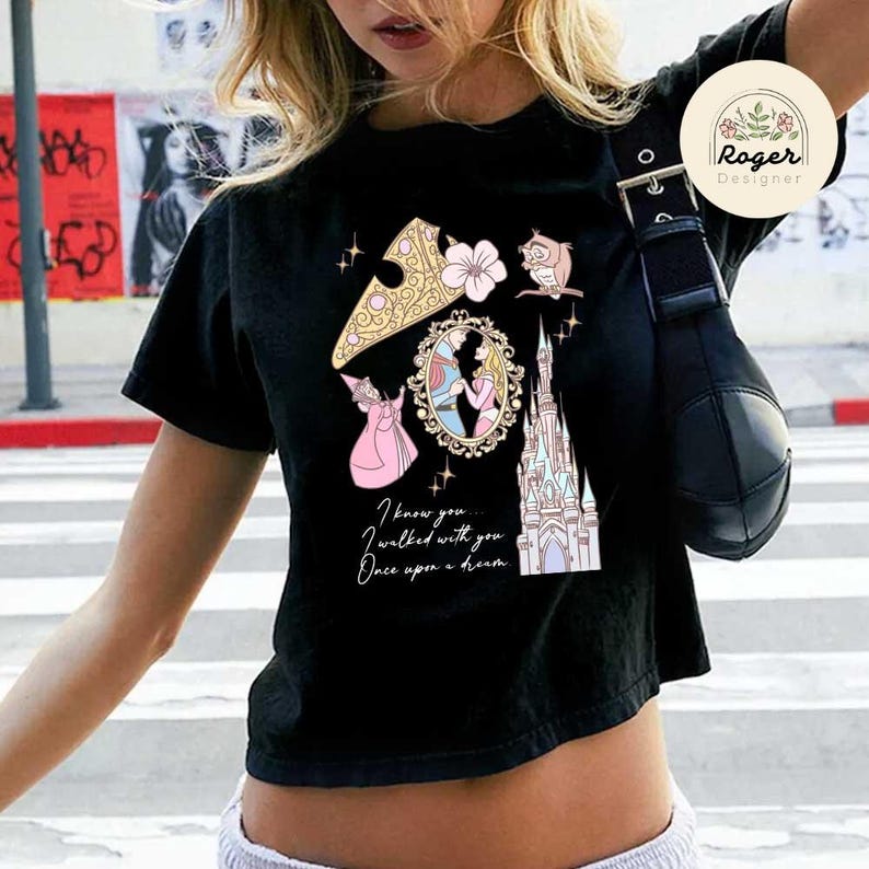 Może przedstawiać: Czarny t-shirt z kolorową grafiką przedstawiającą zamek, księżniczkę i sowę. Tekst "I know you... I walked with you... Once upon a dream" jest wydrukowany poniżej. Logo Roger Designer w prawym g&oacute;rnym rogu.