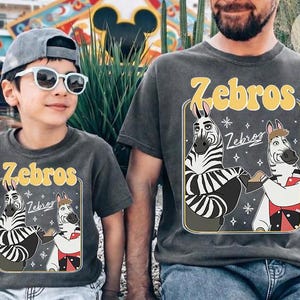 Pu&ograve; includere: Due magliette grigio antracite abbinate con la scritta "Zebros" in giallo, con zebre dei cartoni animati. Una &egrave; indossata da un bambino con occhiali da sole e un berretto grigio. L'altra &egrave; indossata da un adulto. Le magliette sono un set divertente e coordinato.