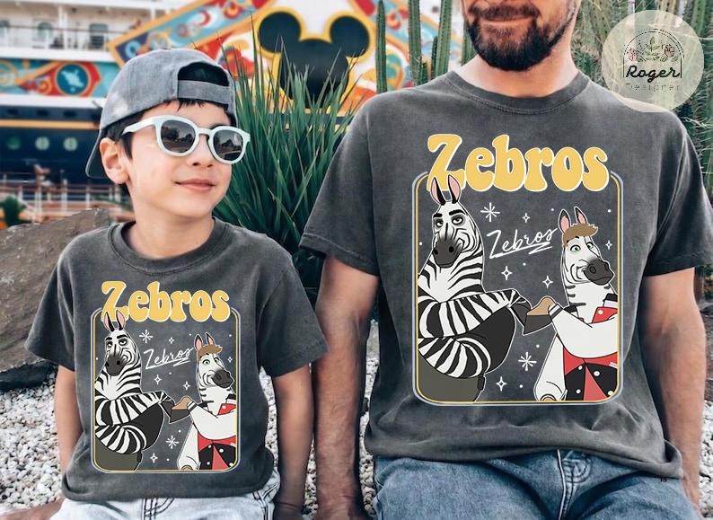 Pu&ograve; includere: Due magliette grigio antracite abbinate con la scritta "Zebros" in giallo, con zebre dei cartoni animati. Una &egrave; indossata da un bambino con occhiali da sole e un berretto grigio. L'altra &egrave; indossata da un adulto. Le magliette sono un set divertente e coordinato.