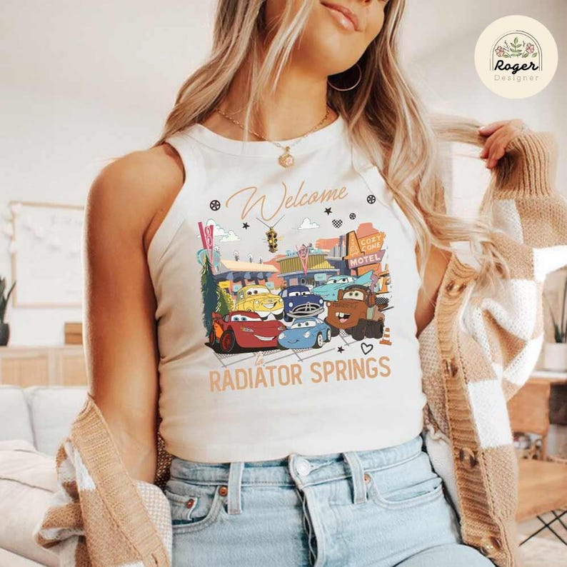 May include: Cream-colored tank top featuring a colorful graphic of characters from the movie Cars in front of a motel. The text "Welcome to Radiator Springs" is printed below the graphic.