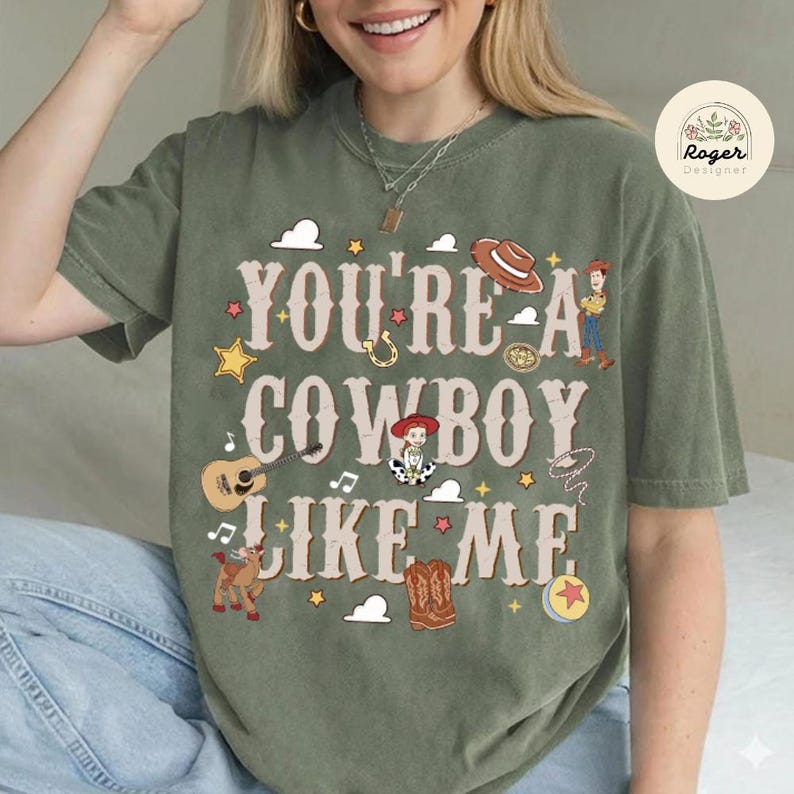 Może przedstawiać: Oliwkowozielony t-shirt z kr&oacute;tkim rękawem z napisem "YOU'RE A COWBOY LIKE ME" czcionką w stylu western. Wz&oacute;r zawiera ilustracje kapelusza kowbojskiego, gitary, konia, but&oacute;w, piłki oraz postaci z serii Toy Story na nadruku graficznym.