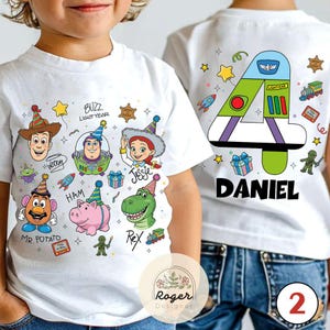 Puede incluir: Camisetas blancas con gr&aacute;ficos coloridos de personajes de Toy Story. Una camiseta presenta a Woody, Buzz Lightyear, Jessie, Sr. Potato, Ham y Rex. La otra camiseta tiene un gran n&uacute;mero 4 con "DANIEL" debajo y gr&aacute;ficos tem&aacute;ticos de Toy Story.