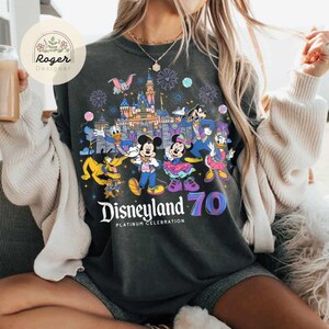 K&ouml;nnte beinhalten: Ein dunkelgraues T-Shirt mit einem grafischen Aufdruck von Mickey Mouse und seinen Freunden, die das 70-j&auml;hrige Jubil&auml;um von Disneyland feiern. Der Aufdruck zeigt das Disneyland-Schloss, Feuerwerk und den Text "Disneyland - Platinum Celebration 70".