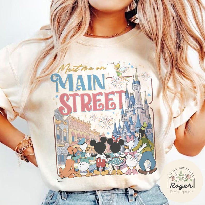 May include: Cream-colored sweatshirt featuring the text "Meet me on Main Street" above a graphic of Disney characters and Cinderella's castle. The design includes Mickey and Minnie Mouse, Donald and Daisy Duck, and Goofy.