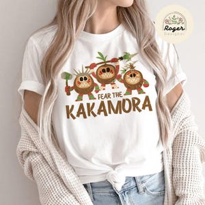 Puede incluir: Camiseta blanca con un gr&aacute;fico de tres personajes de coco de dibujos animados con el texto "Fear the Kakamora".