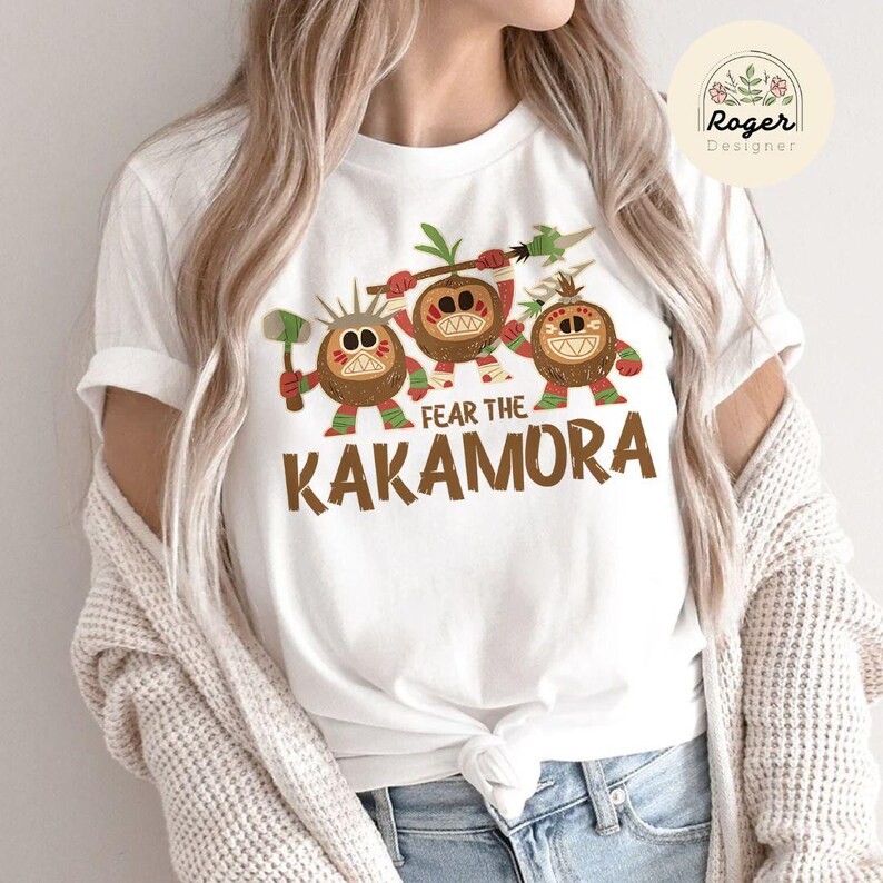 Puede incluir: Camiseta blanca con un gr&aacute;fico de tres personajes de coco de dibujos animados con el texto "Fear the Kakamora".