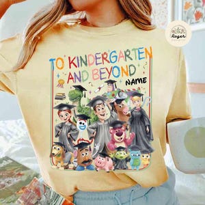 Peut inclure: T-shirt jaune clair avec un motif color&eacute;. Le motif comprend le texte "TO KINDERGARTEN AND BEYOND" et des personnages de dessins anim&eacute;s. Il y a un espace pour un nom. Le t-shirt a un col rond.