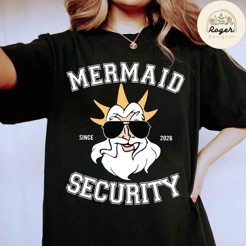 May include: Black t-shirt with the words "MERMAID SECURITY" in white block letters. The design features a cartoon illustration of a bearded figure wearing sunglasses and a crown. The text "SINCE 2026" is also included.