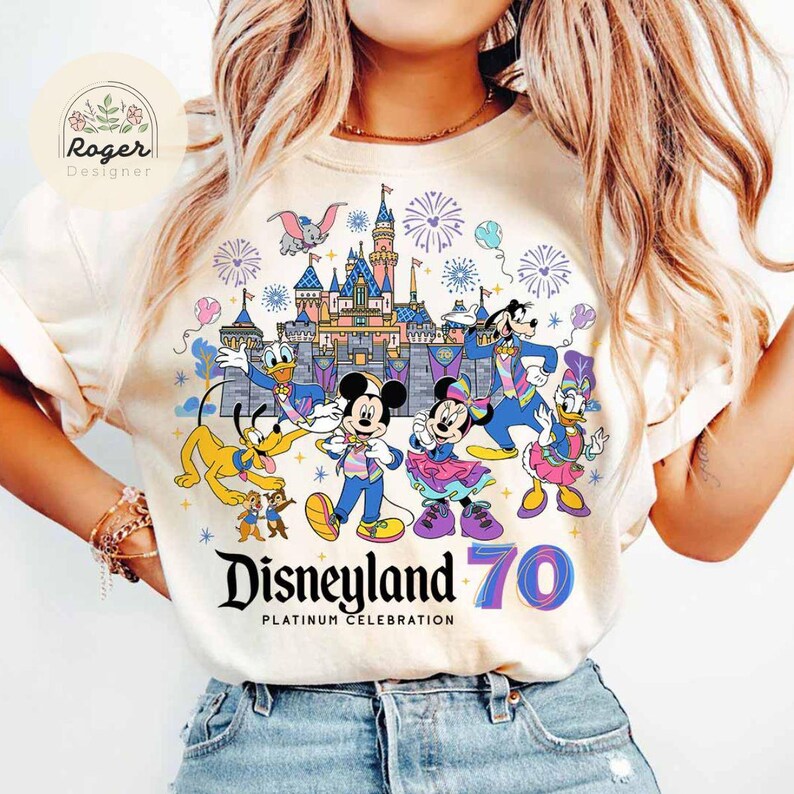 K&ouml;nnte beinhalten: Ein wei&szlig;es T-Shirt mit einer bunten Grafik von Mickey Mouse, Minnie Mouse, Donald Duck, Goofy und anderen Disney-Charakteren, die das 70-j&auml;hrige Jubil&auml;um von Disneyland feiern. Die Grafik enth&auml;lt den Text "Disneyland 70 Platinum Celebration".