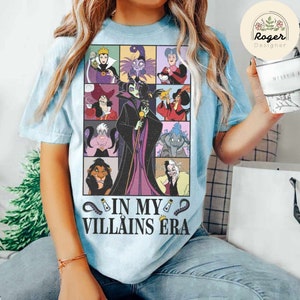 Puede incluir: Una camiseta azul claro con un gr&aacute;fico de villanos de Disney. Los villanos est&aacute;n en un patr&oacute;n de cuadr&iacute;cula e incluyen a Mal&eacute;fica, &Uacute;rsula, Cruella de Vil, y m&aacute;s. El texto "In My Villains Era" est&aacute; impreso debajo del gr&aacute;fico.