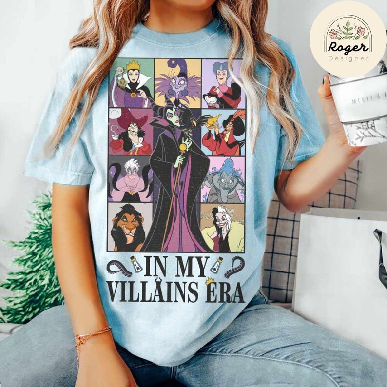 Puede incluir: Una camiseta azul claro con un gr&aacute;fico de villanos de Disney. Los villanos est&aacute;n en un patr&oacute;n de cuadr&iacute;cula e incluyen a Mal&eacute;fica, &Uacute;rsula, Cruella de Vil, y m&aacute;s. El texto "In My Villains Era" est&aacute; impreso debajo del gr&aacute;fico.