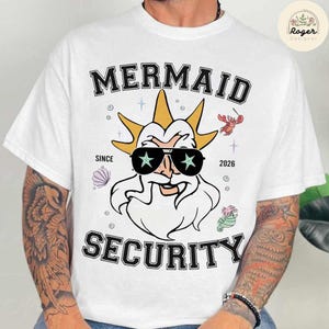 May include: White t-shirt featuring a cartoon illustration of a sea god wearing sunglasses with star-shaped lenses. The shirt has the words "MERMAID SECURITY" and "SINCE 2026" printed on it, along with other sea-themed graphics.