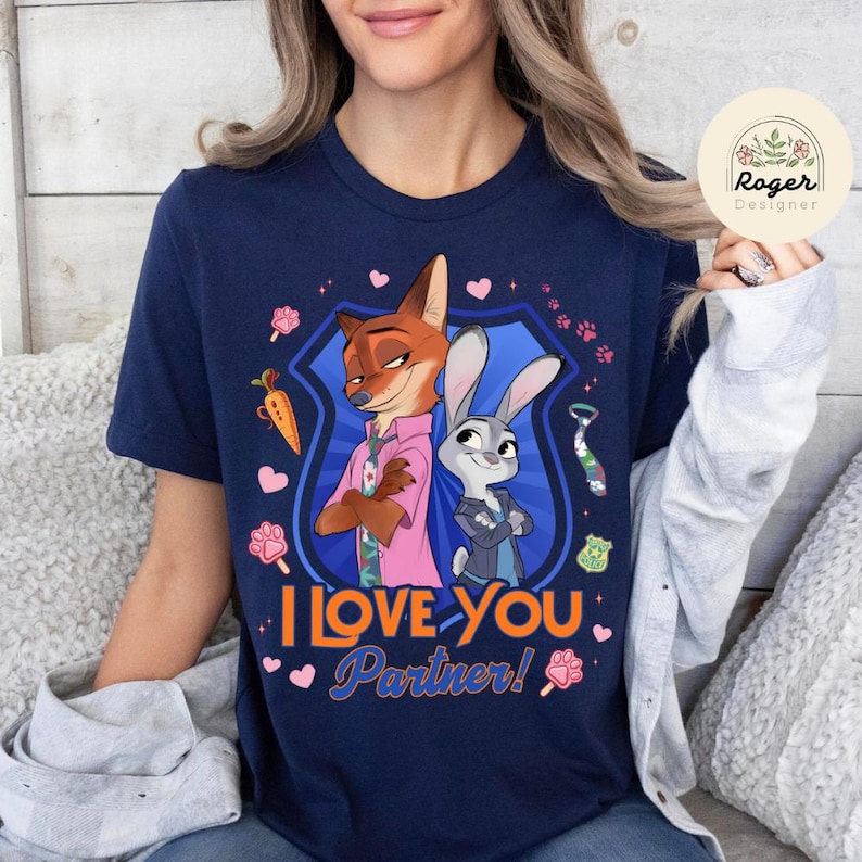 Pu&ograve; includere: T-shirt blu navy con un'illustrazione a cartoni animati di Nick Wilde e Judy Hopps di Zootropolis, con la scritta "I Love You Partner!". Il design include cuori, impronte di zampe e una carota. La maglietta &egrave; girocollo.