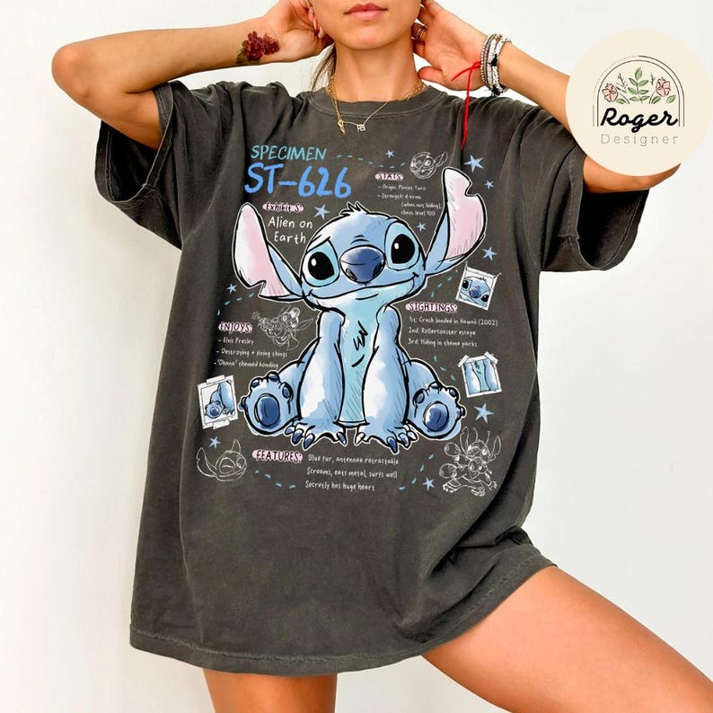 May include: Dark gray t-shirt featuring a blue cartoon character with large ears and the text "SPECIMEN ST-626 Alien on Earth." The design includes character details and scientific-style annotations. A Roger Designer logo is visible.
