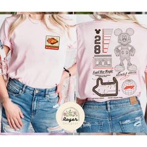 May include: A light pink t-shirt with a Formula 1 racing theme. The front features a small patch with a race car graphic. The back displays a Mickey Mouse outline, the number 28, and the text "Fuel the Magic" and "Mickey Mouse".