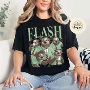 May include: Black t-shirt with a graphic of five sloths wearing green shirts and orange striped ties, holding mugs that read "YOU WANT IT WHEN?". The word "FLASH" is printed above the sloths in green.