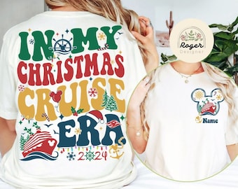 Puede incluir: Camiseta color crema con un diseño gráfico colorido. El diseño presenta el texto "IN MY CHRISTMAS CRUISE ERA 2024" con ilustraciones náuticas y navideñas. Un diseño más pequeño en la parte delantera incluye una cabeza de Mickey Mouse con un crucero.