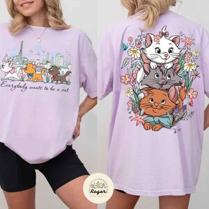 May include: A lavender t-shirt with a graphic of three cartoon cats from the movie The Aristocats. The cats are stacked on top of each other and surrounded by flowers. The text "Everybody wants to be a cat" is printed on the front of the shirt.