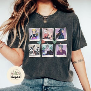 May include: A dark grey t-shirt featuring a vintage-style print of six Disney villains in Polaroid frames. The villains include Maleficent, Ursula, Cruella de Vil, Evil Queen, Lady Tremaine, and Queen of Hearts. The shirt has a distressed look and is ideal for fans of Disney.