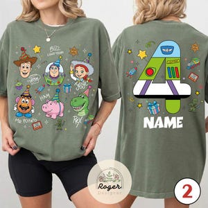 Puede incluir: Camiseta verde oliva con personajes de dibujos animados de Toy Story. La parte delantera muestra a Woody, Buzz Lightyear, Jessie, Sr. Potato, Ham y Rex. La parte trasera muestra un gran n&uacute;mero 4 con un dise&ntilde;o de Buzz Lightyear y la palabra "NAME".