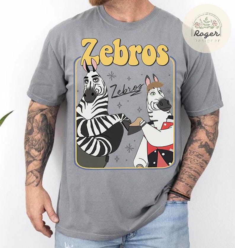 Pu&ograve; includere: T-shirt grigia con un design a cartoni animati di due zebre e la scritta "Zebros". Le zebre sono in una cornice rettangolare con un bordo giallo. La maglietta &egrave; realizzata in un materiale morbido e confortevole.