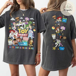 May include: A charcoal gray t-shirt featuring Toy Story characters on the front and back. The front displays the Toy Story logo, the text 'YOU'VE GOT A FRIEND IN ME', and various characters. The back shows a vertical arrangement of characters.