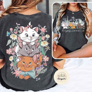 May include: A black t-shirt with a vintage look featuring a stack of three cartoon cats with flowers. The text "Everybody wants to be a cat" is printed on the front of the shirt.