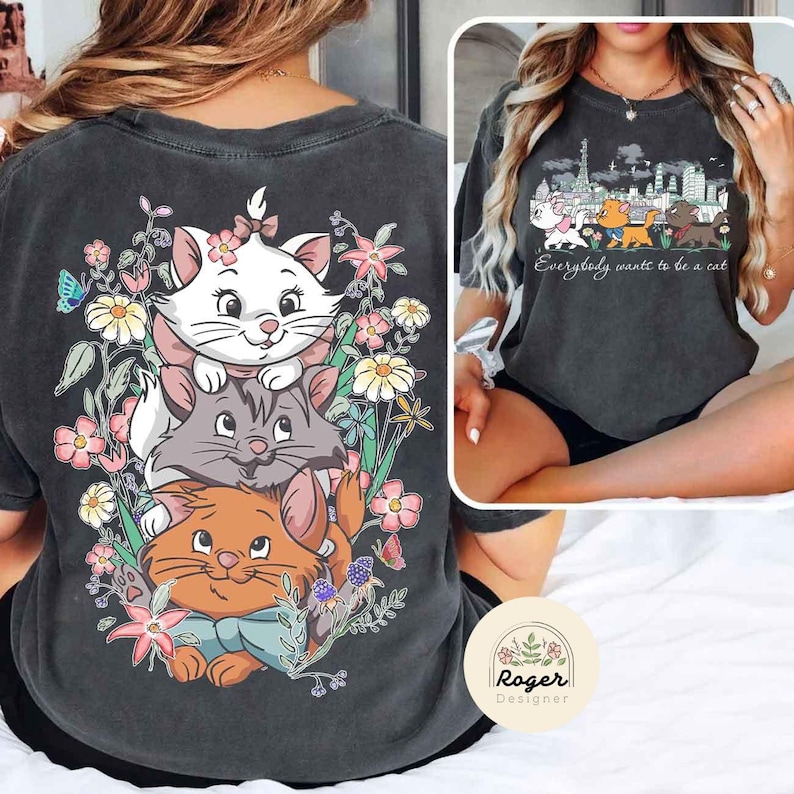 May include: A black t-shirt with a vintage look featuring a stack of three cartoon cats with flowers. The text "Everybody wants to be a cat" is printed on the front of the shirt.