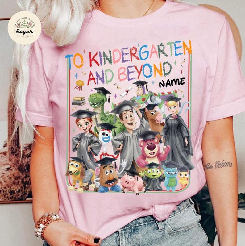Peut inclure: T-shirt rose clair avec l'inscription multicolore "TO KINDERGARTEN AND BEYOND". Le motif pr&eacute;sente des personnages de dessins anim&eacute;s portant des toges et des coiffes de fin d'&eacute;tudes. Un espace est pr&eacute;vu pour un nom.