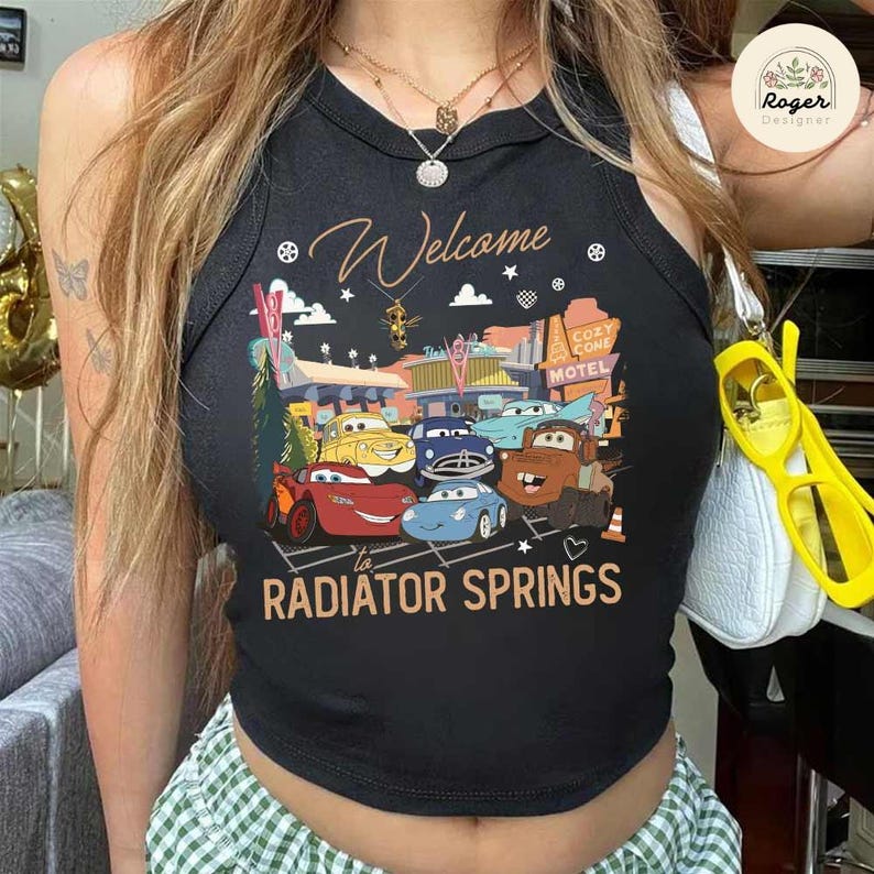 May include: Black tank top featuring a colorful graphic of characters from the movie Cars, with the text "Welcome to Radiator Springs." The design includes various cars and the Cozy Cone Motel.