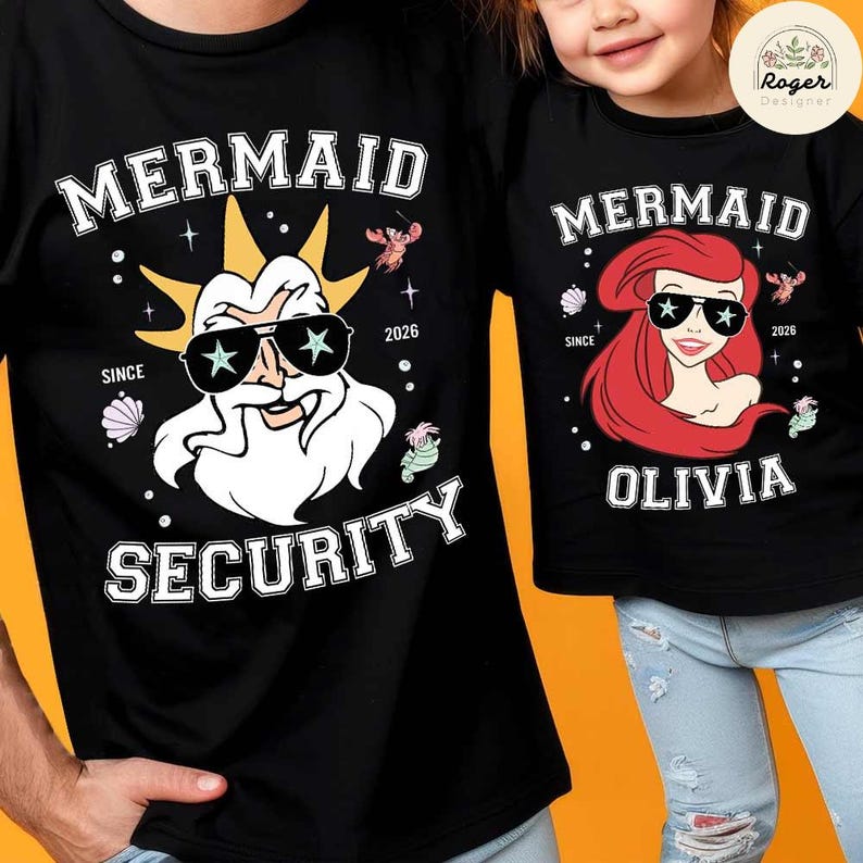 May include: Black t-shirts with matching designs. One shirt features a cartoon of a bearded man wearing sunglasses with the words "MERMAID SECURITY" and "2026". The other shirt has a cartoon of a mermaid with the name "OLIVIA" and the words "MERMAID" and "2026".