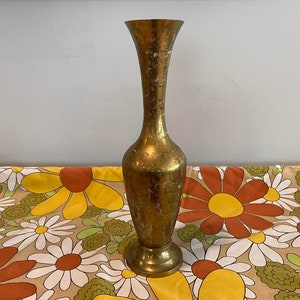 May include: A gold metal vase with an intricate floral design. The vase has a tall, slender neck and a round base.