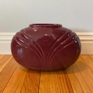 Puede incluir: Un jarrón grande de cerámica de color burdeos, de forma ovalada, con un acabado brillante y un diseño decorativo en forma de abanico.