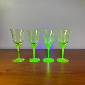 Puede incluir: Un conjunto de cuatro copas de color amarillo neón translúcido dispuestas en fila. Cada copa presenta un tallo delgado, una base circular y un cuenco acampanado con una sutil textura acanalada vertical y pequeños puntos azules en el exterior.