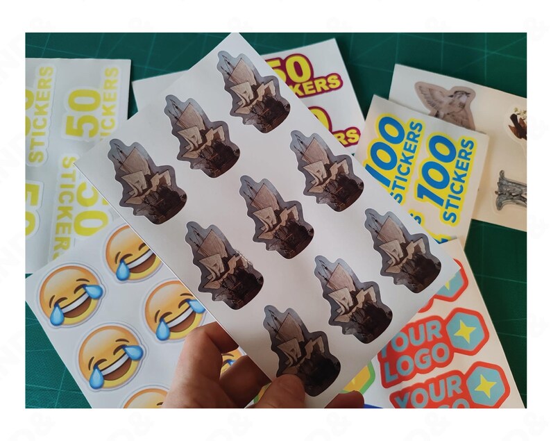 May include: Sheets of stickers featuring various designs. One sheet displays multiple stickers with a brown and beige illustration. Other sheets show stickers with the text "50 STICKERS" and "100 STICKERS". Additional stickers have a laughing emoji and a logo design.