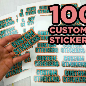 May include: Sheets of custom stickers with the text "CUSTOM STICKERS" in a turquoise and orange design. The number "100" is displayed in a large pink font. One sticker is held in a hand.