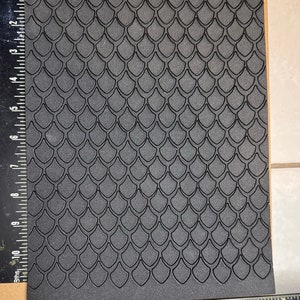 Op de afbeelding: Een zwarte schuimplaat met een reli&euml;fpatroon van overlappende schubben. De plaat is ongeveer 20 cm bij 28 cm.